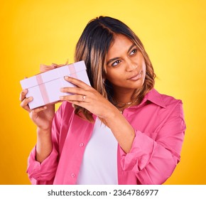 Woman, curious and excited with gift, surprise and happiness on a yellow studio background. Person, girl and model with a ribbon, present and box with package, birthday and thinking with giveaway - Shutterstock ID 2364786977