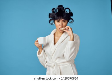    woman with curlers on her head in a bathrobe is having breakfast on a blue background                             - Powered by Shutterstock