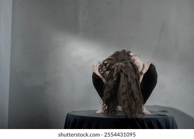 A woman curls up introspectively on a table, suggesting deep thought. The artistic use of shadows and muted tones enhances the piece’s contemplative nature. - Powered by Shutterstock