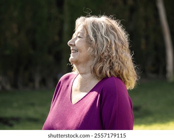 A woman with curly hair enjoys a sunny day in a lush garden. She laughs warmly, radiating happiness and tranquility in a serene setting. - Powered by Shutterstock