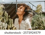 Woman with curly hair laughing outdoors, surrounded by cacti and sunlight. Joyful expression, curly hair, and bright sunlight create a lively scene. Woman image photography.