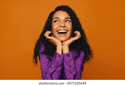 Woman with curly hair on a orange background smiles in a cheerful headshot. The portrait features hands and a fun, dreamy expression with a pensive touch. - Powered by Shutterstock