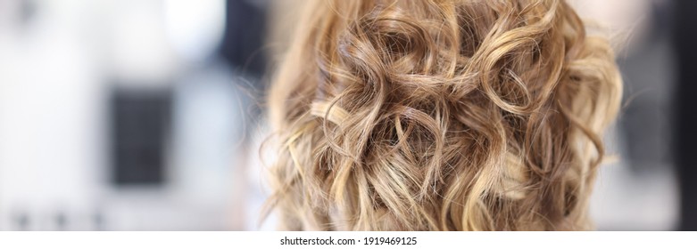 Une femme aux cheveux bouclés s'assoit dans le salon de beauté en arrière-plan. Concept de coiffure professionnelle en gros plan.
