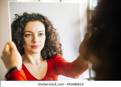 Woman With Curly Hair Standing In Front Of  Large Mirror And Smiling