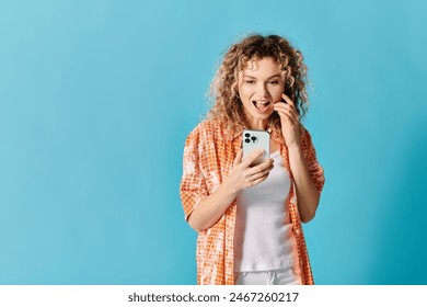 Woman with curly hair standing, looking at phone against blue backdrop - Powered by Shutterstock