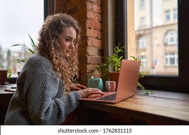 Frau mit lockigen Haaren, die mit einer Tasse Tee auf ihrem Laptop arbeitet. Arbeit und Tee genießen