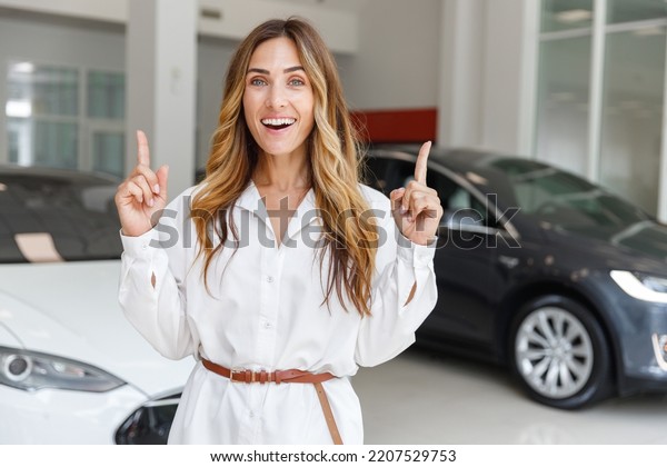 Woman customer buyer client in white shirt hold\
index finger up with great new idea choose auto want buy new\
automobile in car showroom vehicle salon dealership store motor\
show indoor. Sales\
concept