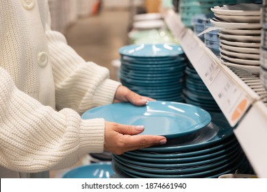 Woman customer choosing and buying blue clay dishes plates, dinner utensil for her kitchen in houseware store or supermarket. Shopping concept.