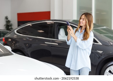 Woman Customer Female Buyer Client Wears Blue Shirt Do Photo On Mobile Cell Phone Choose Auto Want Buy New Automobile In Car Showroom Vehicle Salon Dealership Store Motor Show Indoor. Sales Concept