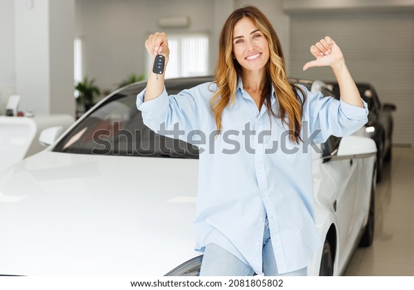 Woman customer female buyer client wears blue\
shirt point thumb finger on keys chooses auto wants to buy new\
automobile in car showroom vehicle salon dealership store motor\
show indoor. Sales\
concept