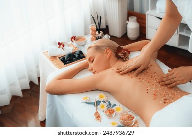 Woman customer having exfoliation treatment in luxury spa salon with warmth candle light ambient. Salt scrub beauty treatment in health spa body scrub. Quiescent - Powered by Shutterstock