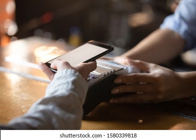 Woman customer holding phone near nfc terminal make contactless mobile payment using app concept in store restaurant, female buyer client pay with cellphone via pos machine on counter, close up view