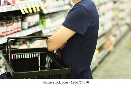 Woman Customer Shopping At Grocery Pharmacy. Female Holding Basket Trying To Decide Which Products To Buy. Retail Healthcare Medicine, Vitamins, And Supplements.
