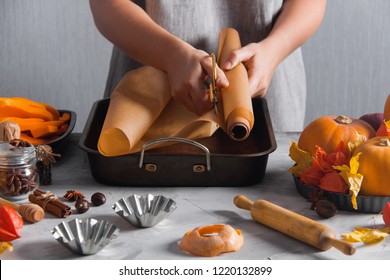 Woman cut baking baking paper in iron form, cooking baking. Autumn time, pumpkins, physalis, yellow dry leaves, spices, cinnamon, anise, cloves, kitchen tools, wooden rolling, pin, nutmegs.