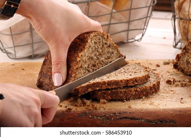 Woman cut whole grain bread on a wooden board