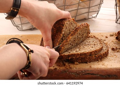Woman cut whole grain bread on a wooden board