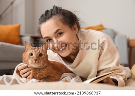 Woman with cute ginger cat and book at home on autumn day
