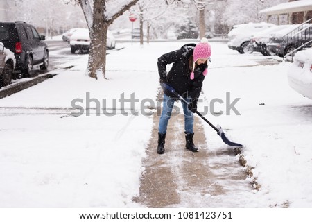 Woman in cute pink hat shovelling / shoveling snow