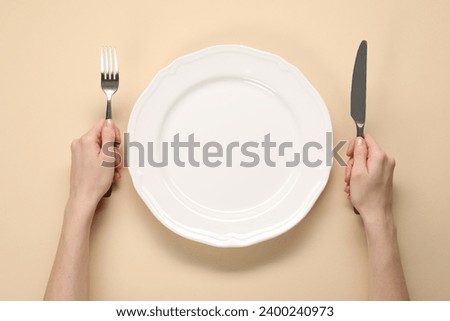 Woman with cutlery and empty plate at beige table, top view