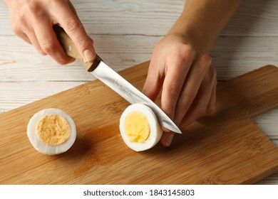 Woman cuts boiled egg on board on white wooden background - Powered by Shutterstock