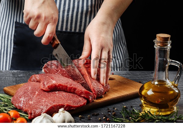 Woman cuts a piece of beef with a knife on a\
cutting board close-up.