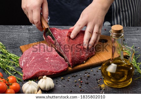 A woman cuts a piece of juicy beef into steaks. Meat and hands with a knife close-up.