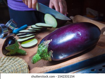 Woman Cutting Beautiful Purple Eggplants In Kitchen With A Sharp Knife. Ripe Aubergine.