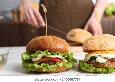 Woman cutting bun at white marble table, focus on delicious vegetarian burgers - Powered by Shutterstock