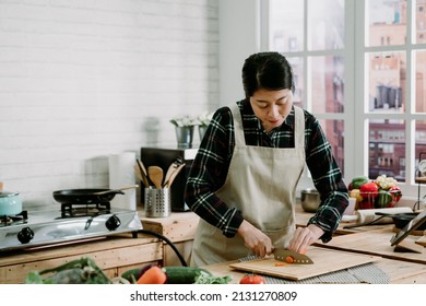 Woman Cutting Carrot On Wooden Island Table In Modern Kitchen At Home. Smiling Asian Chinese Lady Watching Tv Show On Digital Tablet And Cooking Dinner Preparing Healthy Meal With Fresh Vegetables.