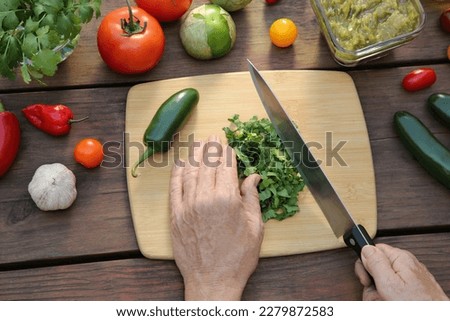 Woman cutting cilantro for salsa sauce at wooden table, top view