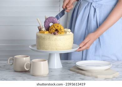 Woman cutting delicious cake decorated with sweets at white marble table, closeup