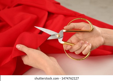Woman cutting fabric with sharp scissors at white table, closeup