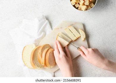 Woman cutting fresh bread for croutons on white background