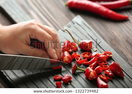 Woman cutting fresh chili peppers on wooden board, closeup
