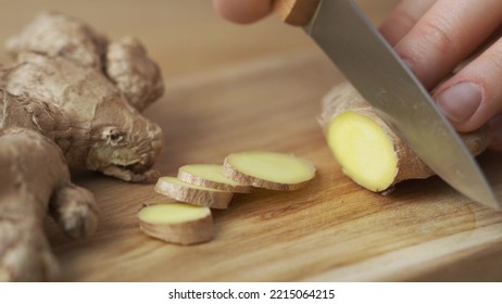 Woman Cutting Fresh Ginger Root On Kitchen Table, Close Up