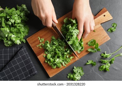 Woman cutting fresh green cilantro at black table, top view