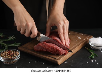 Woman cutting fresh raw meat at black table, closeup - Powered by Shutterstock