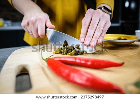 Woman cutting green spicy pepper jalapeno on wooden cutting board in the kitchen. Defocused. High quality photo