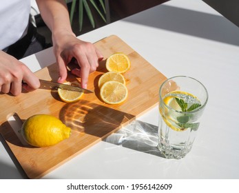 Woman cutting lemon on wooden board. Detox water with mint and lemon. Refreshing summer drink. Wellness, diet, healthy eating concept - Powered by Shutterstock