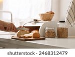 Woman cutting loaf near wooden bread basket at white marble table in kitchen, closeup