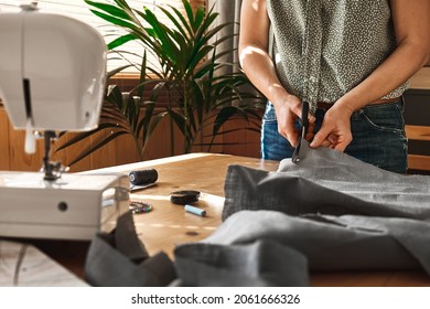 Woman Cutting Out A Pattern Paper In Linen Fabric. Seamstress Sewing On The Sewing Machine In Small Studio. Fashion Atelier, Tailoring, Handmade Clothes Concept. Slow Fashion Conscious Consumption