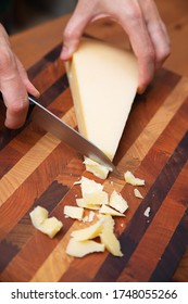Mujer cortando parmesano en tablero de madera. Delicioso queso para el desayuno. Captura de estudio. Vista en ángulo. El concepto de la comida y la cocina lácteas en casa para folletos y pancartas