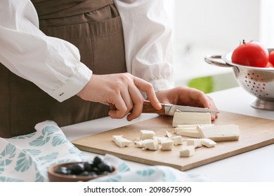 Woman Cutting Tasty Feta Cheese On Table In Kitchen, Closeup