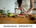 A woman is cutting vegetables on a wooden cutting board. The vegetables include carrots and peppers