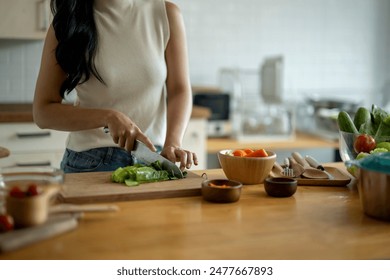 A woman is cutting vegetables on a wooden cutting board. The vegetables include carrots, celery, and cucumbers - Powered by Shutterstock