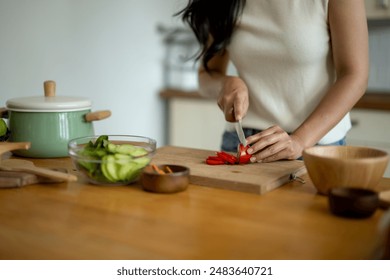 A woman is cutting vegetables on a wooden cutting board. The vegetables include carrots and peppers - Powered by Shutterstock