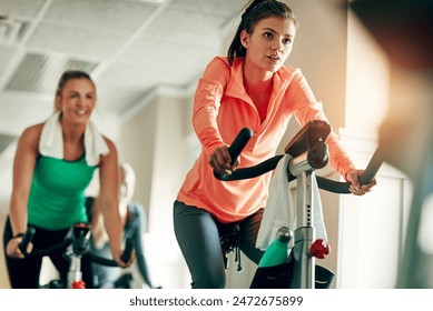 Woman, cycling and workout with spin class at gym for cardio exercise or indoor training together. Active female person or group of cyclists riding on equipment or bicycle for fitness at health club - Powered by Shutterstock