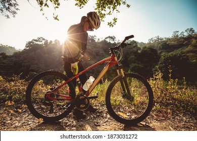 Woman cyclist adjust the seat height cycling on sunrise winter forest trail - Powered by Shutterstock