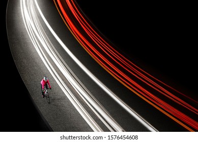 Woman Cyclist In Bright Pink Jacket Riding The Bike On The Night Road With Cars Light Trails. Healthy Lifestyle And Urban Active Sport Concept.