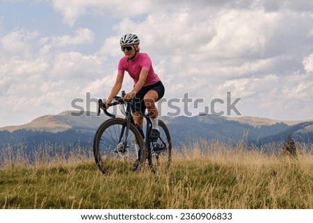 Woman cyclist in cycling kit and helmet riding a gravel bicycle on mountain road.Sportswoman cycling in the beautiful natural surroundings. Cyclist practicing on gravel road.Bucegi Mountains, Romania.